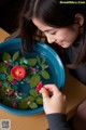 A young girl holding a red flower in a blue bowl.