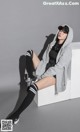 A woman sitting on a white cube wearing a gray hoodie and black shorts.