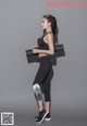A woman in a black sports bra top and black leggings holding a yoga mat.