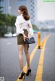 A woman in a white blouse and a brown skirt is standing on the street.