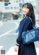 A young woman in a school uniform holding a blue bag.