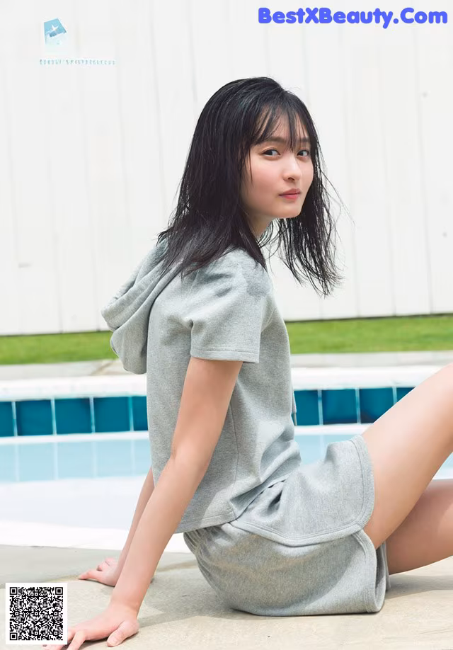 A woman sitting on the ground next to a swimming pool.