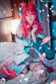 A woman with pink hair sitting on a bed.