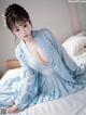 A woman in a blue dress sitting on a bed.